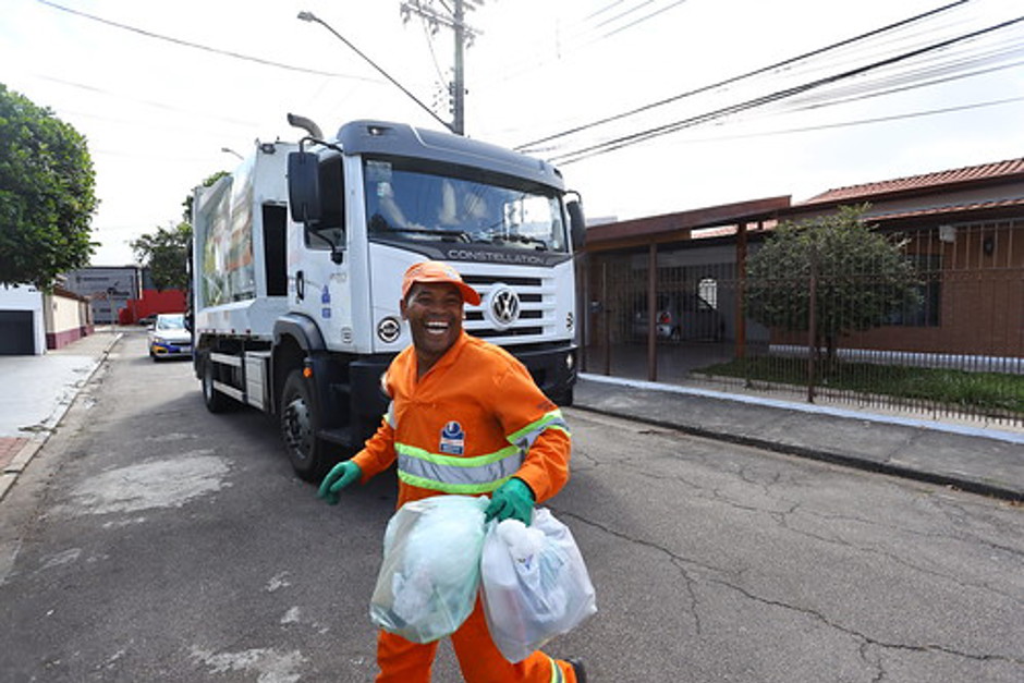 Agente ambiental sorrindo enquanto realiza a coleta de resíduos