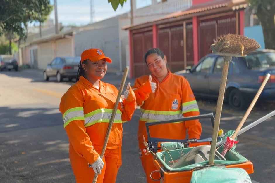 Duas colaboradoras da equipe de varrição da Urbam aparecem uniformizadas e sorrindo para a foto