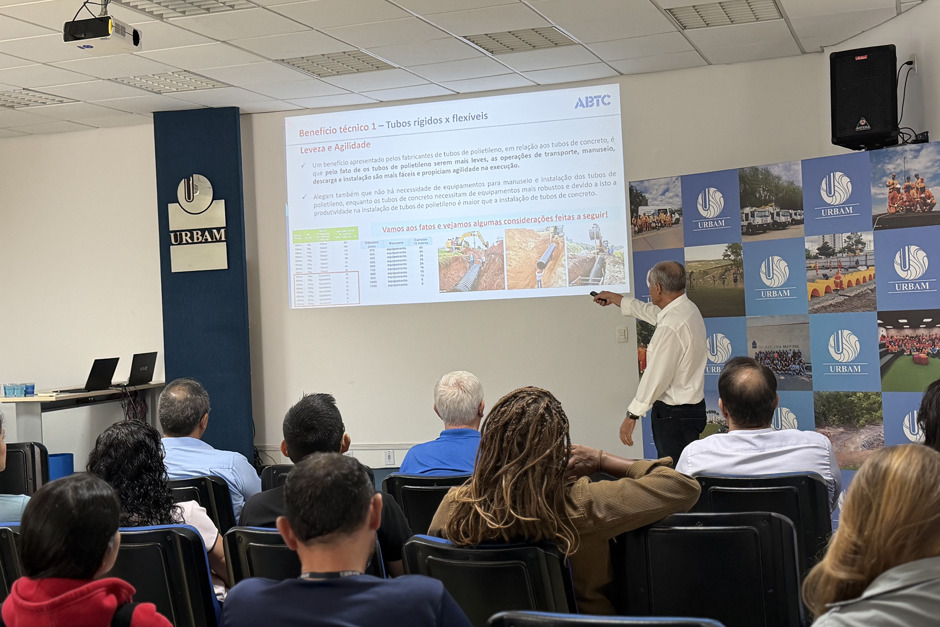 Palestrante na sede da Urbam aponta para estruturas de tubos rígidos, nas cadeiras do auditório estão presentes engenheiros da Urbam e Prefeitura