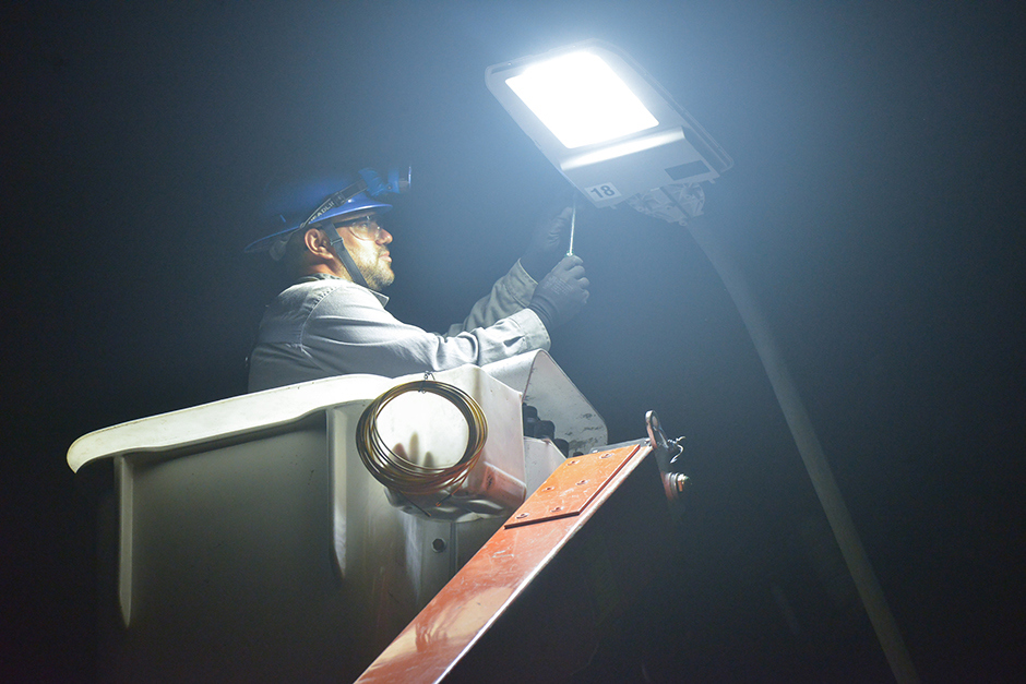 Técnico eletricista faz manutenção em poste de iluminação pública a noite