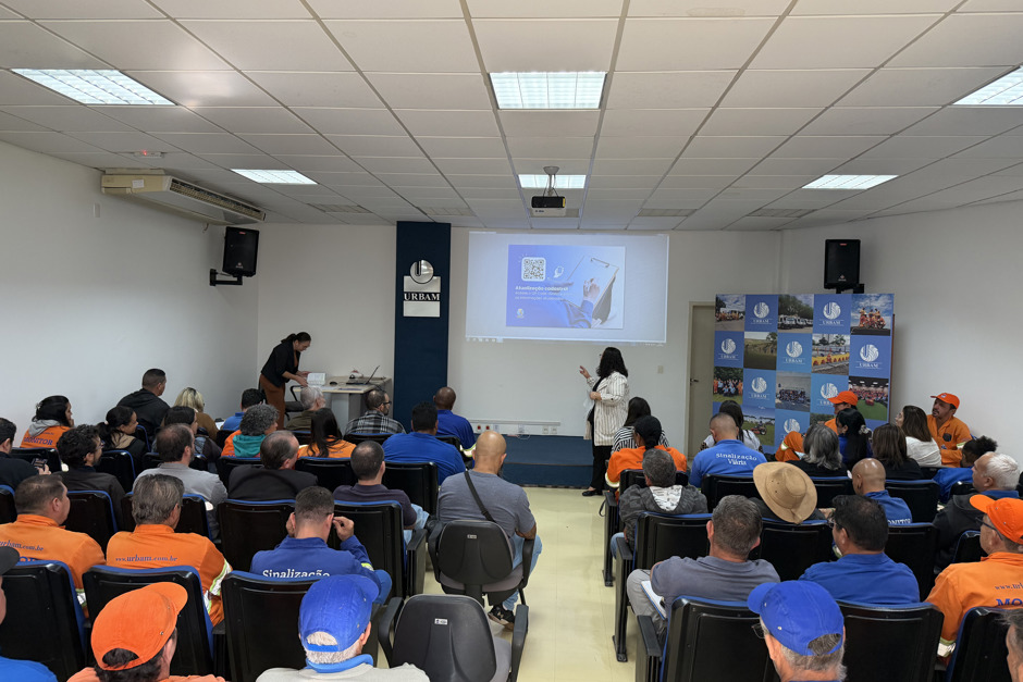 Líderes da Urbam, majoritariamente vestidos de laranja ou azul, se reuniram no auditório da empresa para o treinamento